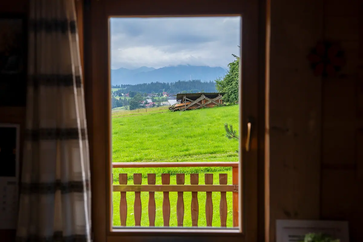 Widok z wnętrza domu przez otwarte drzwi na łąkę i Tatry